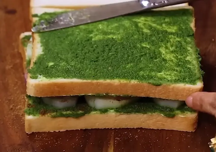 applying green sauce on sandwich