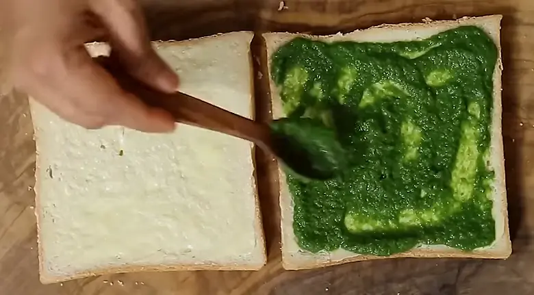 applying green sauce on sandwich